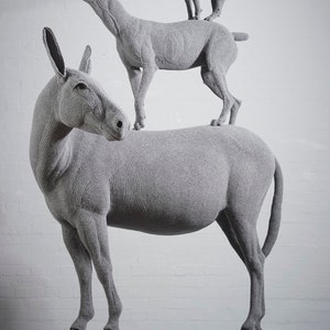 May include: A gray sculpture of a donkey, a wolf, a lion, and a bird stacked on top of each other. The donkey is at the base, with the wolf standing on its back. The lion is on the wolf, and the bird is on the lion.