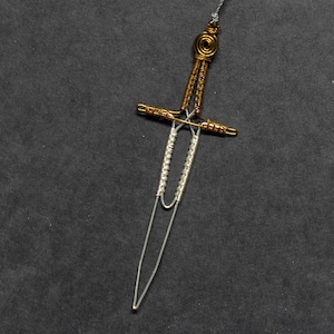 May include: A silver and gold wire sword bookmark. The sword is made of wire and has a gold wire handle.