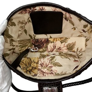 Puede incluir: El interior de un bolso de cuero marr&oacute;n con un forro de estampado floral. El bolso tiene un bolsillo peque&ntilde;o y un cierre de cremallera.