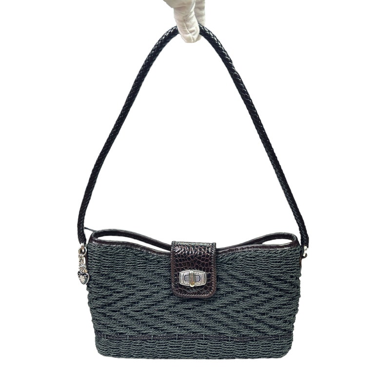 Puede incluir: Un peque&ntilde;o bolso tejido de color gris oscuro con una solapa de cuero marr&oacute;n y un cierre plateado. El bolso tiene una correa de cuero marr&oacute;n y un dije plateado.