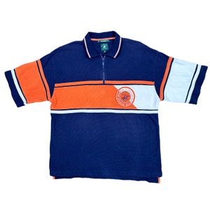 May include: A blue, orange, and white striped short-sleeved polo shirt with a zipper closure. The shirt has a circular logo with a horse and rider on it and the text "Polo Club".