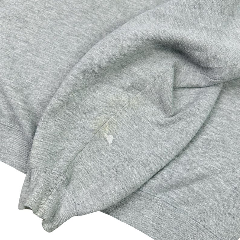 May include: Close-up of a grey sweatshirt sleeve. The sleeve is folded, showing the cuff and a small stain near the elbow. The fabric appears to be a soft, knit material.