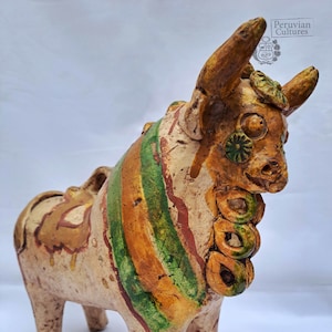 Op de afbeelding: Een keramiek stierenbeeldje met groene, oranje en witte geverfde strepen. De stier heeft een gedetailleerd gezicht met geverfde ogen en een gekrulde staart.