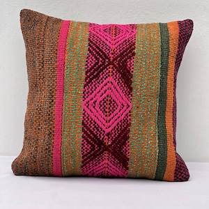 Peut inclure: Un coussin carré avec un motif géométrique coloré. Le coussin est fait de tissu tissé et présente des rayures orange, vertes, roses et brunes.