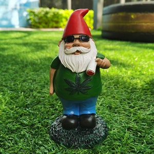 May include: A garden gnome figurine wearing sunglasses and a green shirt with a marijuana leaf design. The gnome is holding a white, rolled-up object in its right hand.