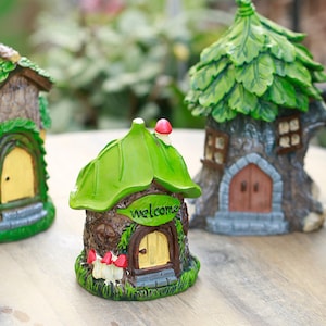 May include: A set of miniature fairy houses with leaf-shaped roofs and wooden doors. The houses are painted in green, brown, and yellow. One house has a sign that says "welcome". The houses are designed to look like they are made of wood and stone.