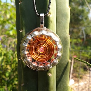 May include: A round pendant necklace with a copper wire spiral and silver beads encased in clear resin. The pendant is hanging from a black cord.