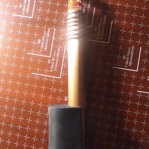 May include: A wooden wand with a clear crystal at the top, wrapped in copper wire. The wand has a black foam grip at the bottom. The wand is 21 cm long and 1.5 cm in diameter.