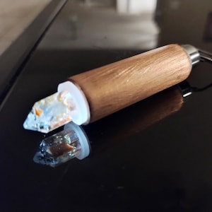 May include: A wooden keychain with a clear crystal attached to the end. The crystal has a gold and white swirl inside.