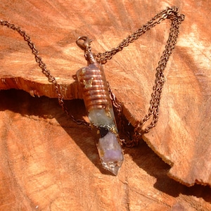 May include: A copper chain necklace with a crystal pendant. The pendant is a clear quartz point with amethyst, black tourmaline, and gold flakes inside. The pendant is wrapped in copper wire.