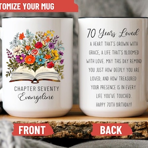 May include: White ceramic mug with a black handle and rim. The front features a floral arrangement atop an open book, with the text "Chapter Seventy Evangeline." The back reads "70 Years Loved" with a birthday message.