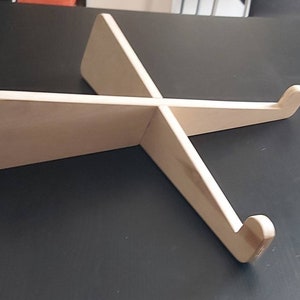 Può includere: Un supporto per laptop in legno di colore chiaro. Il supporto è costruito con due pezzi che si intersecano, formando una forma a X. Il design include supporti curvi per tenere saldamente un laptop. Il supporto è in legno non rifinito.