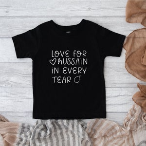 Może przedstawiać: Czarny T-shirt z kr&oacute;tkim rękawem z białym napisem "Love for &hearts; hussain in every tear &hearts;".