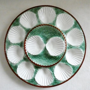 May include: A white ceramic serving dish with a green and brown design. The dish is shaped like a scallop shell and has 12 individual compartments for serving small items.
