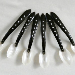 Puede incluir: Juego de seis cucharas de nácar blanco y negro con mangos negros y lunares blancos. Las cucharas están dispuestas en forma de abanico.