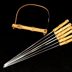 May include: A set of eight bamboo skewers with metal tips. The skewers are tied together with a leather strap and have a bamboo handle.
