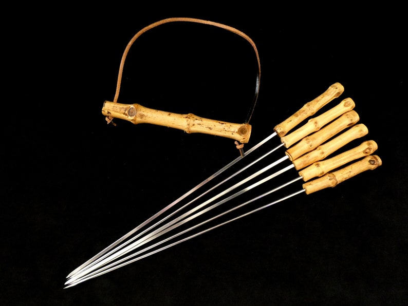 May include: A set of eight bamboo skewers with metal tips. The skewers are tied together with a leather strap and have a bamboo handle.