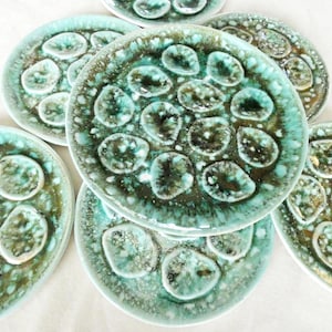 Puede incluir: Un conjunto de platos de cerámica con un diseño único. Los platos presentan un esmalte moteado turquesa y marrón, con detalles ovalados en relieve. Los platos están apilados, mostrando sus cualidades decorativas y funcionales.