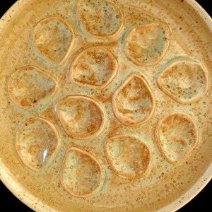 May include: A ceramic serving dish with a textured surface and multiple indentations. The dish is a light beige color with brown and green speckles.