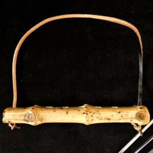 May include: A set of bamboo skewers with a leather strap handle. The skewers are made of natural bamboo and have a light brown color. The handle is made of brown leather and has a loop for hanging.