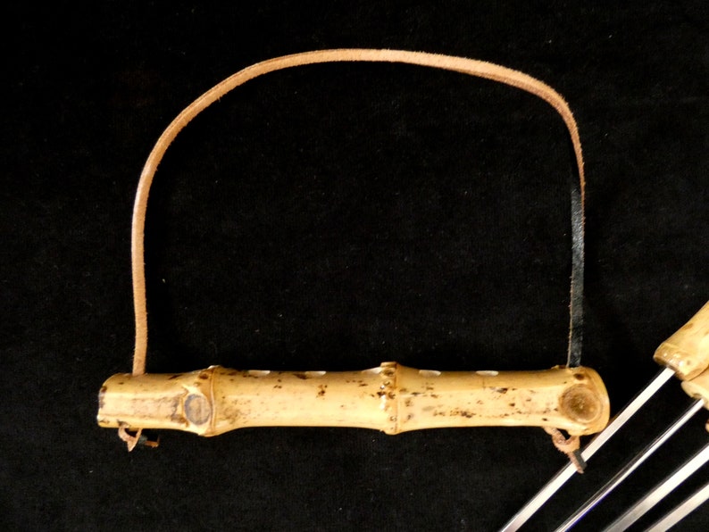 May include: A set of bamboo skewers with a leather strap handle. The skewers are made of natural bamboo and have a light brown color. The handle is made of brown leather and has a loop for hanging.