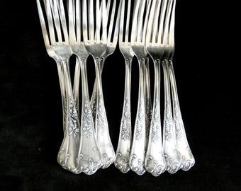 Peut inclure: Ensemble de fourchettes argentées avec des motifs floraux décoratifs sur les manches. Les dents sont fines et parallèles. Les fourchettes sont présentées sur un fond noir, soulignant leur finition polie.