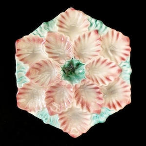 Peut inclure: Une assiette à huîtres en céramique blanche avec un bord festonné et un motif floral. L'assiette comporte huit compartiments individuels pour servir les huîtres.