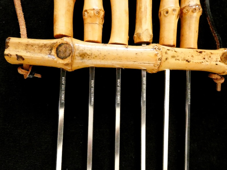May include: A set of six bamboo skewers with stainless steel tips. The skewers are tied together with a brown leather cord. The tips are marked "Stainless Steel Japan".