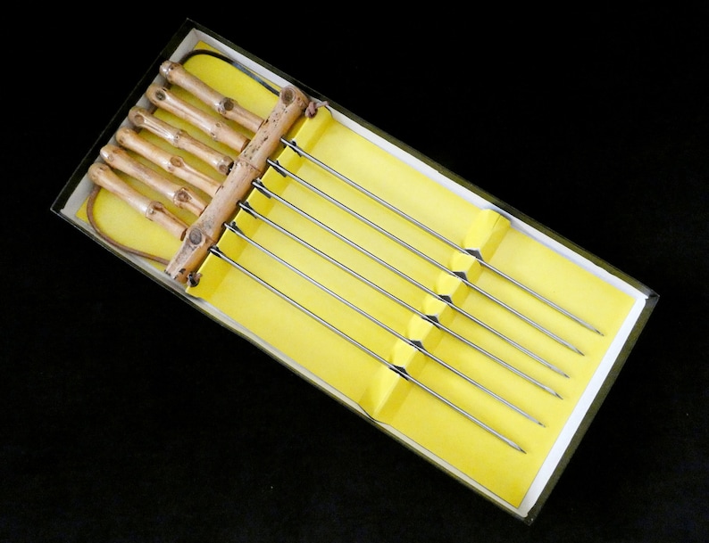 May include: A set of six metal skewers with wooden handles. The skewers are in a yellow box with a white border. The handles are made of natural bamboo.