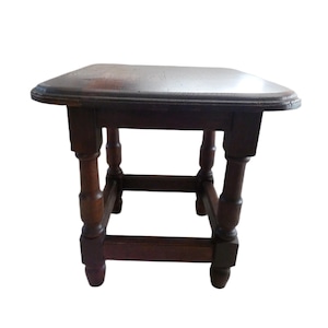 May include: A small, dark brown wooden side table with a square top and turned legs. The table has a classic design, with a slightly rounded edge on the tabletop. The legs are connected by horizontal supports, adding to its stability.