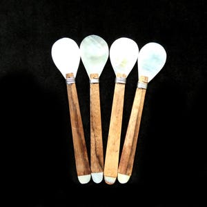 May include: Four serving spoons with pearlescent white spoon heads and wooden handles. The handles are a light brown colour with a silver band where the spoon head connects. The spoon tips are white.