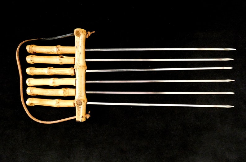 May include: A set of six metal skewers with wooden handles. The skewers are attached to a wooden base with a leather strap.