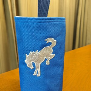 May include: A blue canvas tote bag with a silver glitter embroidered horse design. The bag has a navy blue handle.