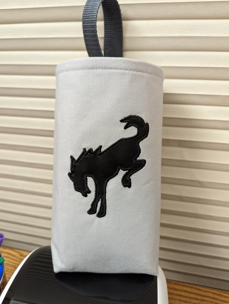 May include: A white canvas bottle holder with a black embroidered running horse design. The holder has a grey fabric loop handle.