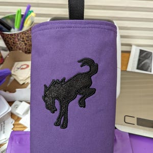 May include: Purple canvas bag with a black embroidered horse design. The bag has a black handle.