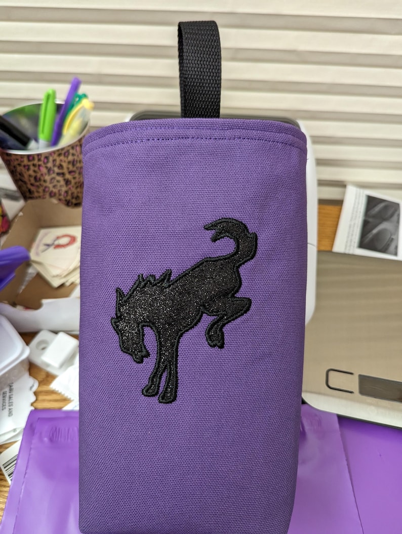 May include: Purple canvas bag with a black embroidered horse design. The bag has a black handle.