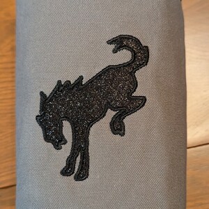 May include: A grey canvas bag with a black embroidered horse design. The bag has a loop handle at the top.