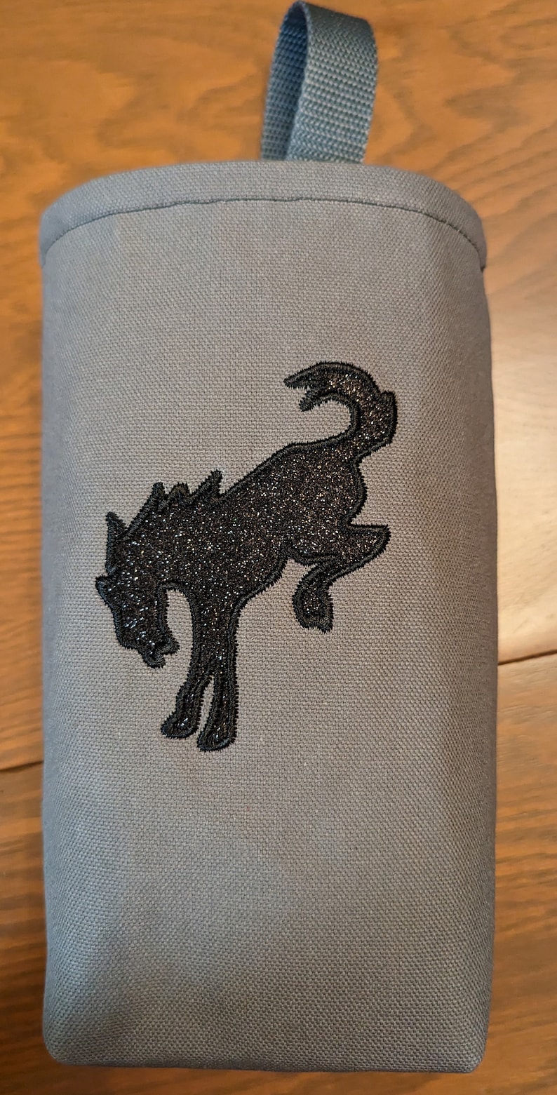 May include: A grey canvas bag with a black embroidered horse design. The bag has a loop handle at the top.