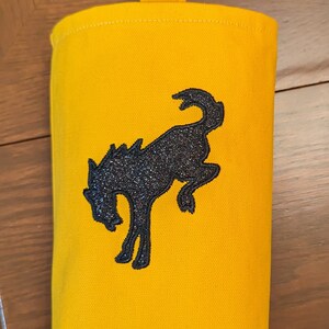 May include: A yellow canvas bag with a black embroidered horse design. The bag has a yellow strap for hanging.