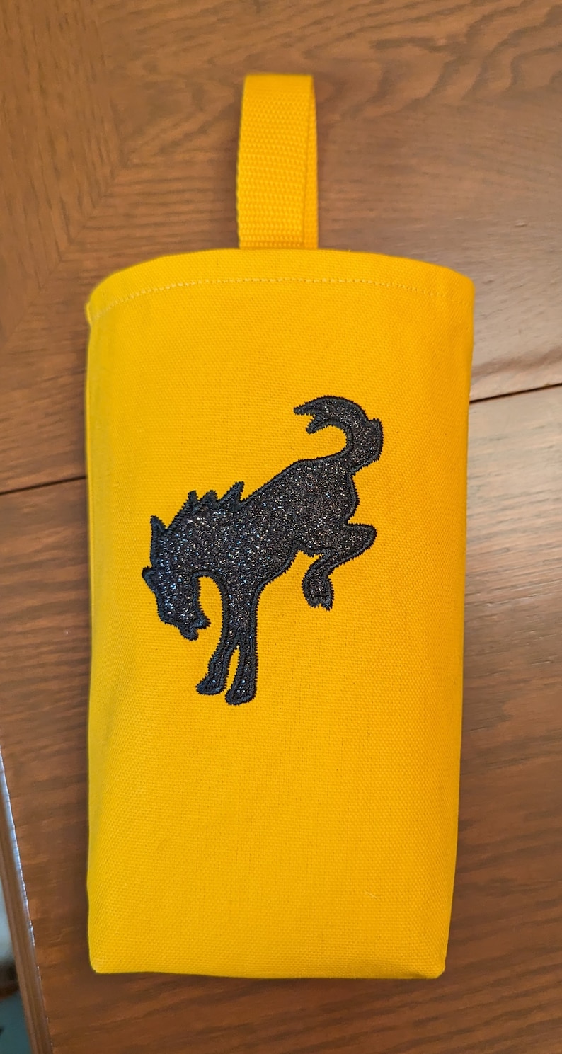 May include: A yellow canvas bag with a black embroidered horse design. The bag has a yellow strap for hanging.