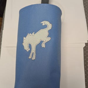 May include: A blue fabric pouch with a white embroidered horse design. The pouch has a black strap at the top.