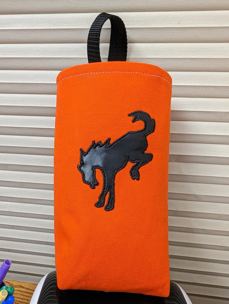 May include: Orange canvas bag with a black handle and a black embroidered silhouette of a bucking horse.