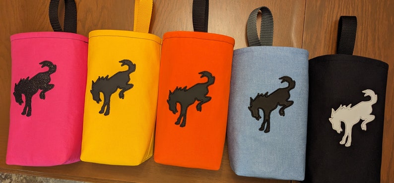 May include: Five fabric pouches with a black horse silhouette design. The pouches are in pink, yellow, orange, light blue, and black. Each pouch has a black loop handle.