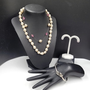 May include: A set of pearl jewelry featuring a long pearl necklace with pink accents, a silver bangle bracelet with heart-shaped accents, and a pair of small pink stud earrings.