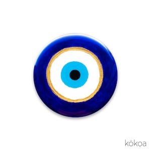 May include: A blue evil eye charm with a white center and a gold ring around the eye. The charm is a popular symbol of protection against bad luck.