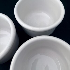 Puede incluir: Primer plano de tres cuencos peque&ntilde;os de cer&aacute;mica blanca. Los cuencos tienen un dise&ntilde;o simple y redondeado con un acabado liso y brillante. Est&aacute;n vac&iacute;os y limpios, lo que sugiere que est&aacute;n listos para usar. Ideal para servir.