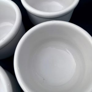 Puede incluir: Primer plano de varios ramequines de cer&aacute;mica blanca. Los ramequines tienen un dise&ntilde;o simple y redondeado con un acabado liso y brillante. Los cuencos est&aacute;n vac&iacute;os y parecen limpios.