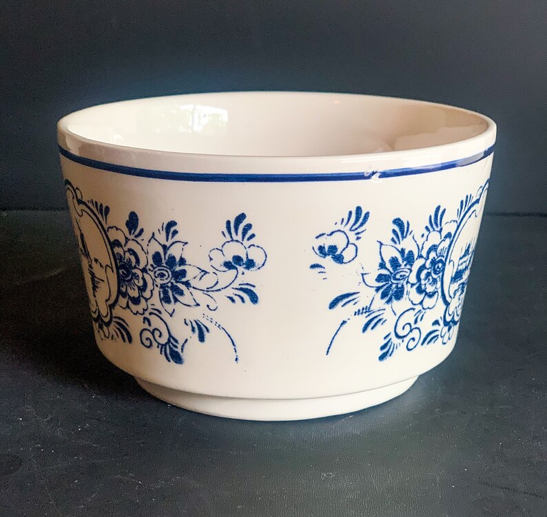 Puede incluir: Un cuenco de cer&aacute;mica blanco con un dise&ntilde;o floral azul. El cuenco tiene una forma ligeramente acampanada con una banda azul alrededor del borde. El patr&oacute;n floral se repite alrededor del exterior del cuenco.