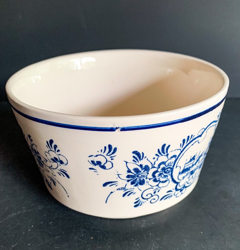 Puede incluir: Cuenco de cer&aacute;mica blanquecina con dise&ntilde;os florales y paisaj&iacute;sticos azules. El cuenco tiene un borde azul y una forma ligeramente inclinada. Los patrones florales son detallados y estilizados, a&ntilde;adiendo un toque decorativo.