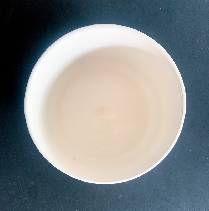 Puede incluir: Vista superior de un cuenco de cer&aacute;mica blanco roto vac&iacute;o. El cuenco tiene una forma redondeada con un interior liso y un exterior ligeramente texturizado. El cuenco est&aacute; sobre un fondo oscuro.